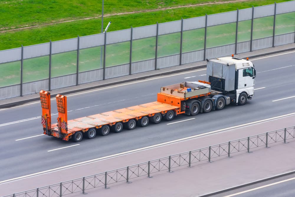 Truck with a trailer and an empty orange long platform rides in the city on the highway