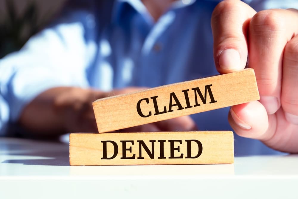person holding word blocks that say 'claim denied'