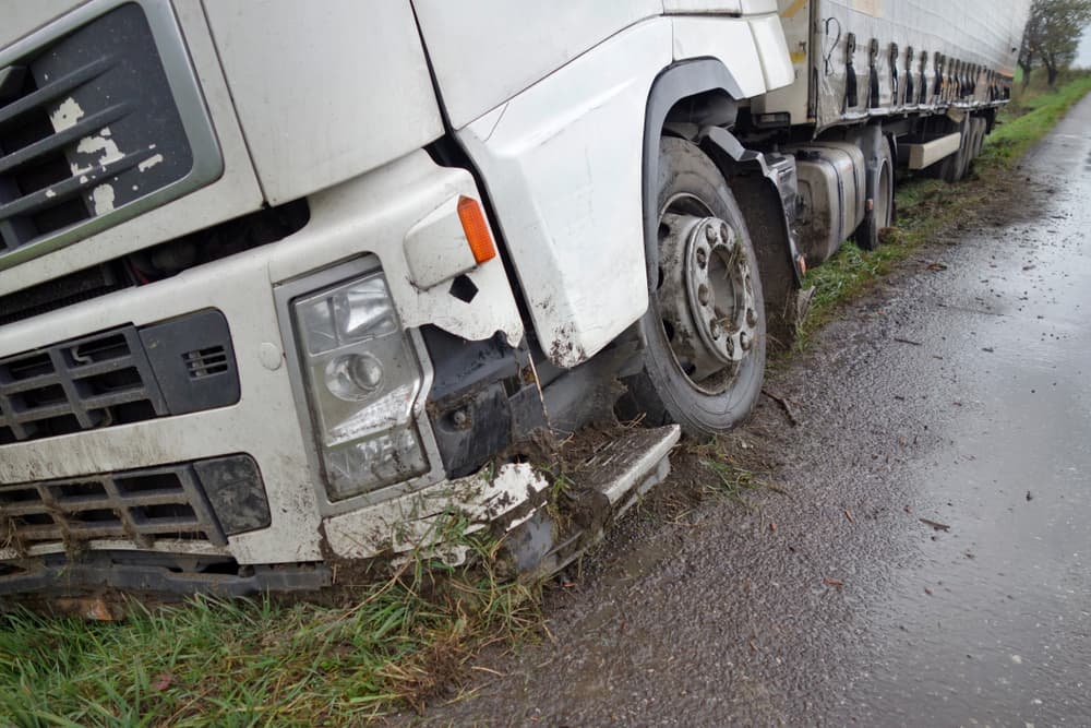 The truck lies in a ditch after the road accident over raining day in autumn time.